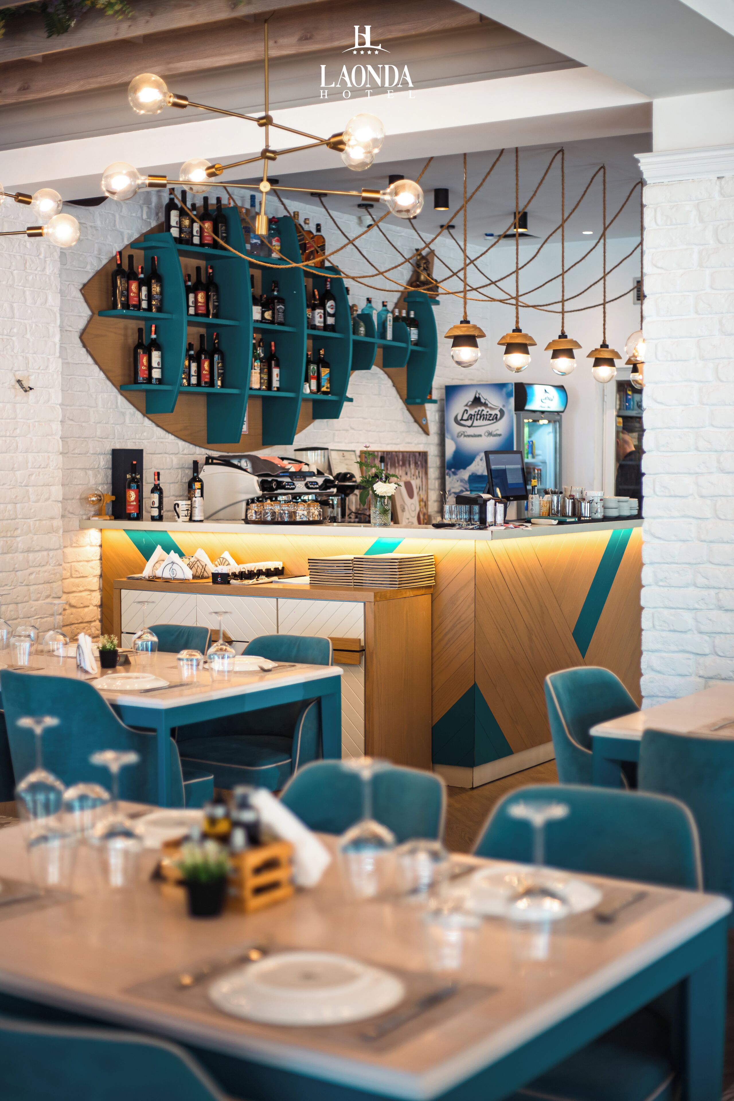 Interior de restaurante com cadeiras cor turquesa, balcão de madeira e luminárias pendentes.