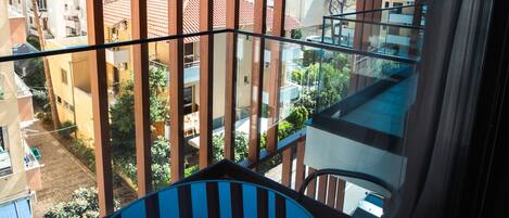 A balcony with a table and chair, overlooking a residential area with buildings and trees.