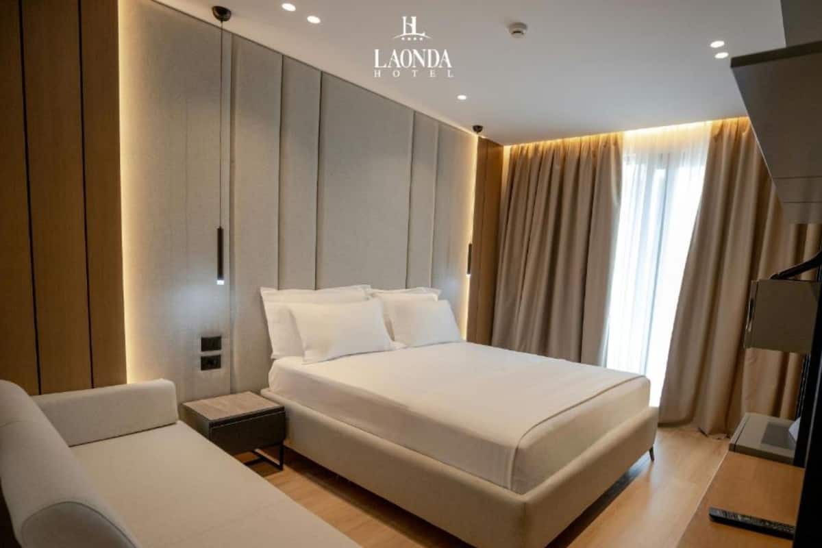 Una habitación de hotel moderna con una cama grande, un sofá, una mesita de noche y un televisor.