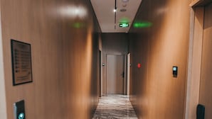 A hallway with wooden walls, a marble floor, and a door at the end. There are signs on the walls and a light fixture on the ceiling. - La Onda Hotel (Durrës)