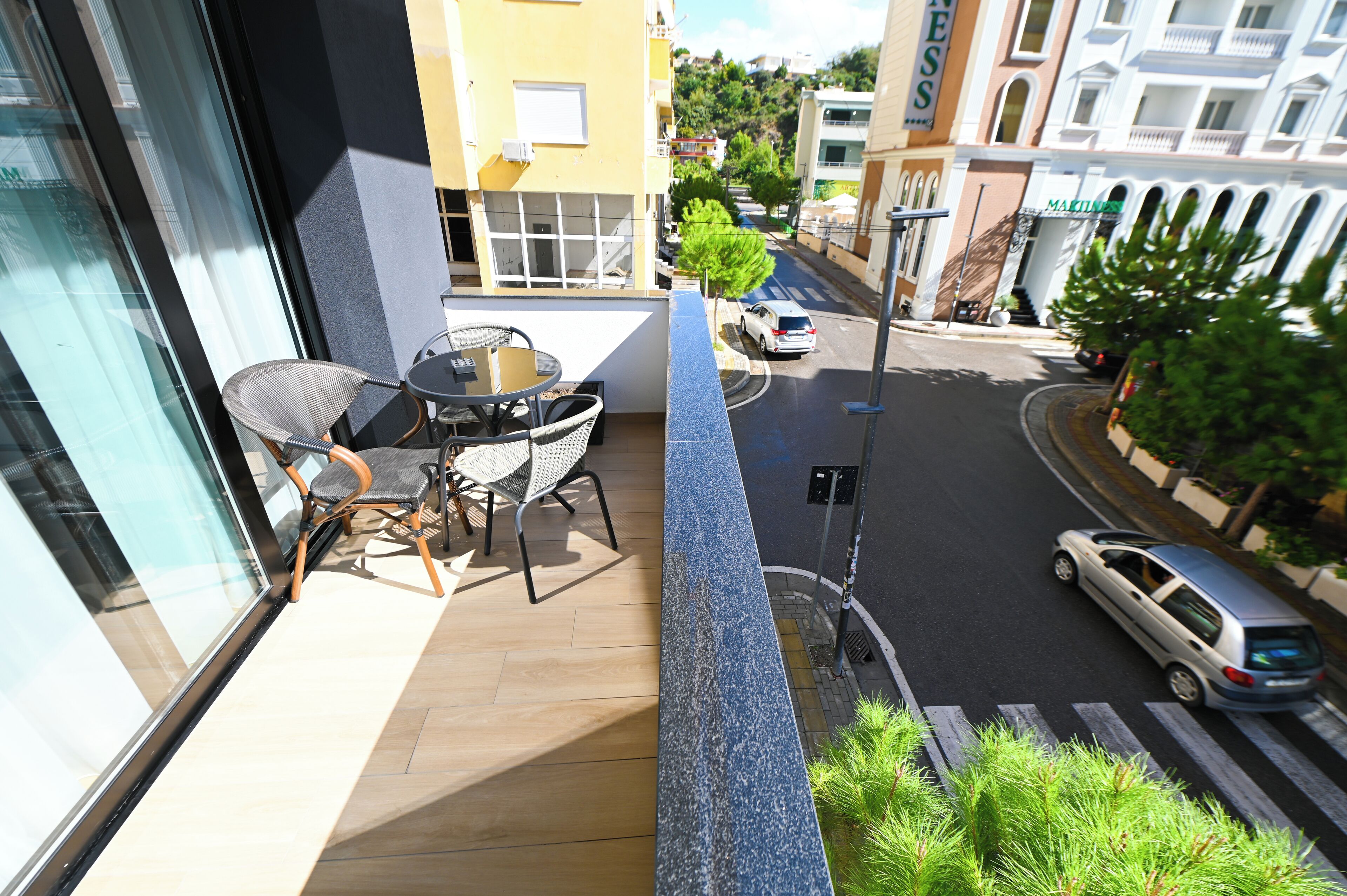 Un balcón con una mesa y sillas, con vistas a una calle con coches y edificios.