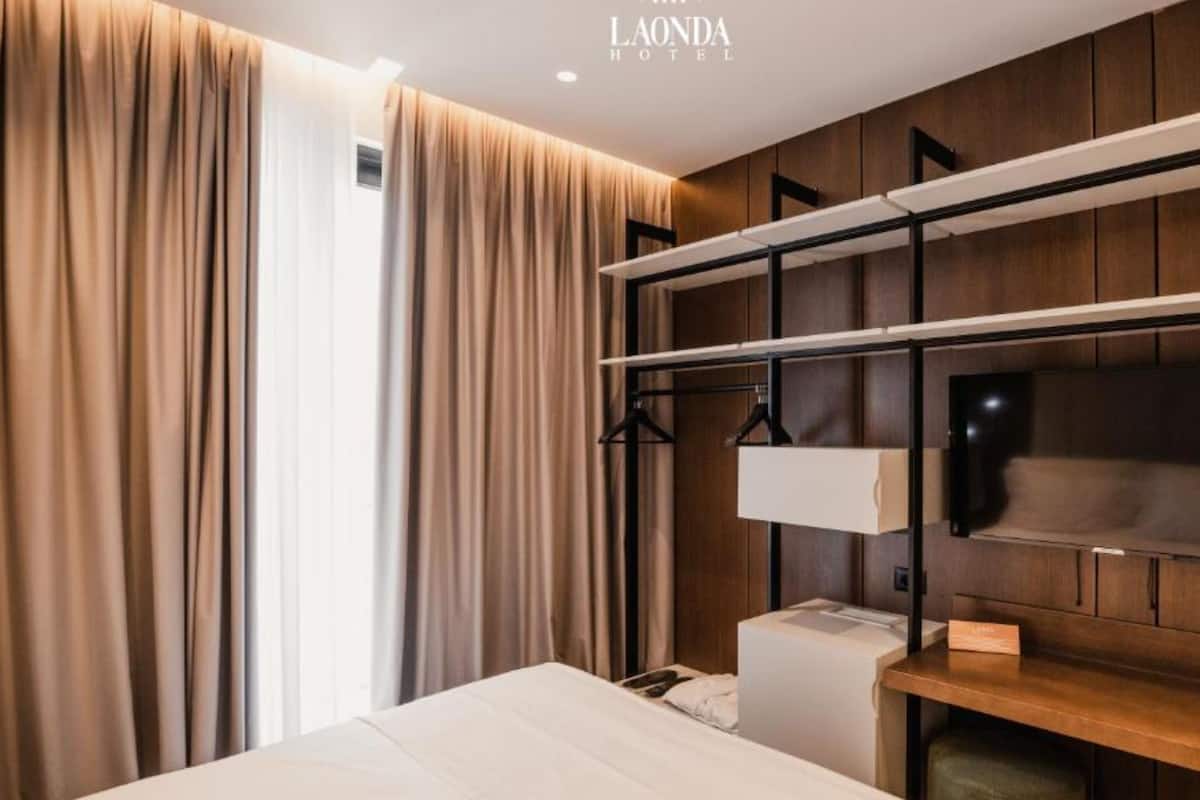 Una habitación de hotel moderna con una cama grande, un armario con espacio para colgar y un televisor de pantalla plana montado en la pared.