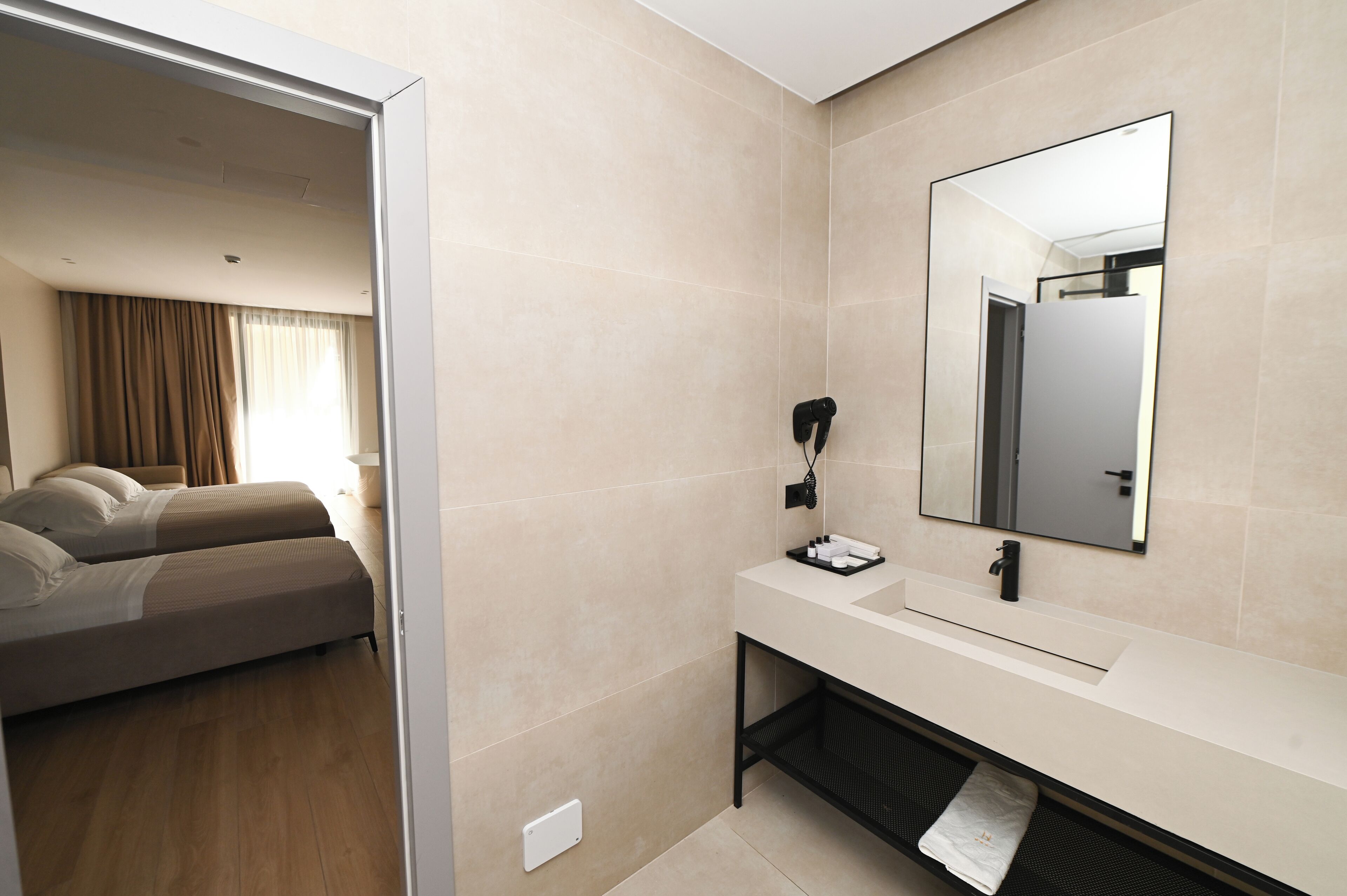 Habitación de hotel con cama, baño con lavabo y espejo, y vista al exterior.