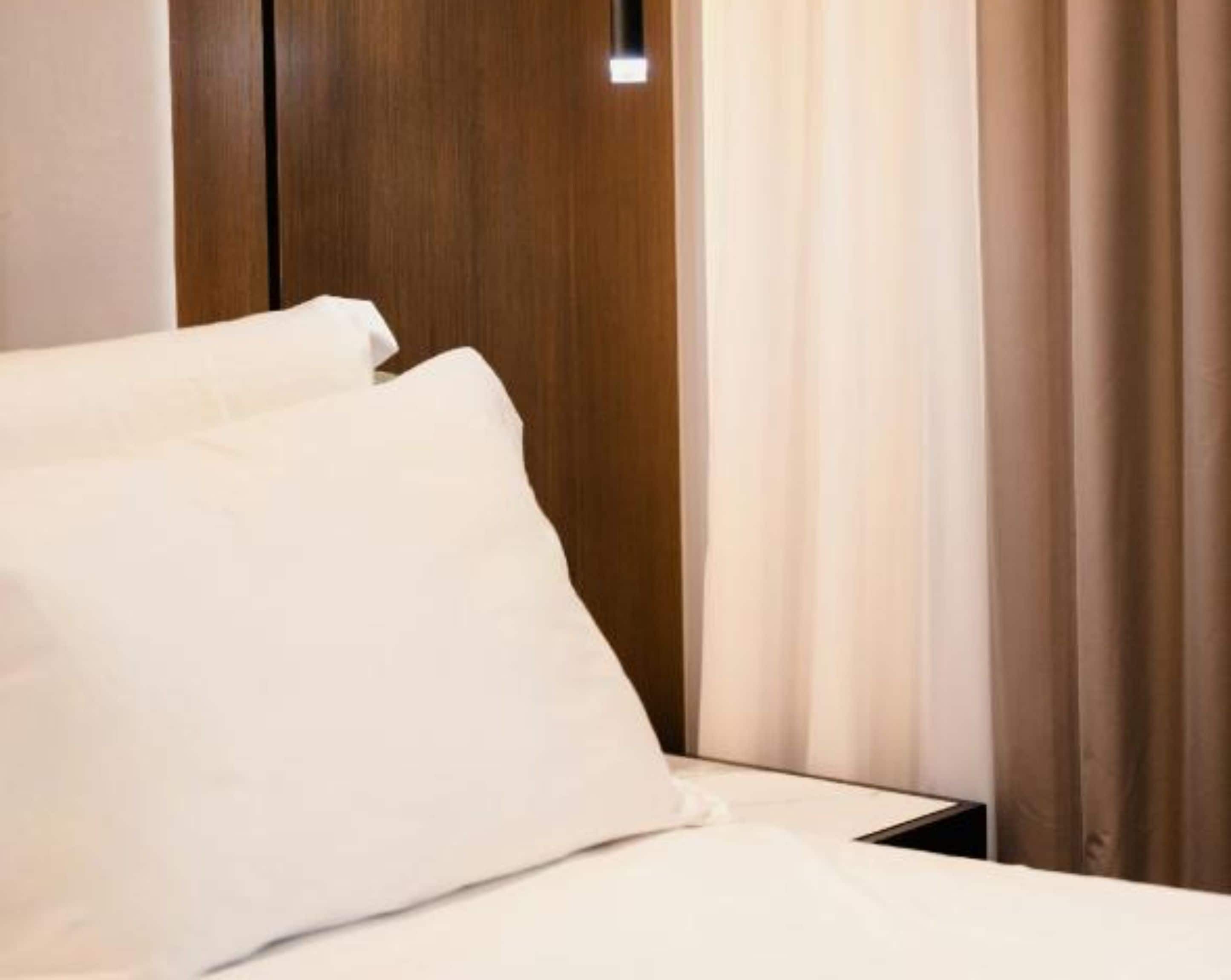Una habitación de hotel con cabecera de madera, ropa de cama blanca y una ventana con cortinas.