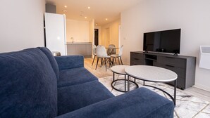 A modern living room with a blue sofa, a round coffee table, and a TV on a cabinet. - GuestReady - Lux getaway in Liverpool (Liverpool)