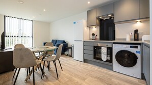 A modern kitchen with a dining area, including a table and chairs, a washing machine, and a microwave. - GuestReady - Lux getaway in Liverpool (Liverpool)