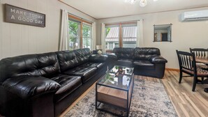 A living room with a black leather sofa, a glass coffee table, and a dining table with chairs. - The Loon at Darling Shores (Alexandria)