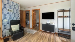 A room with a black leather chair, a TV on a cabinet, wooden flooring, and a patterned wall. - The Loon at Darling Shores (Alexandria)