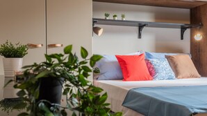 Een slaapkamer met een bed, kamerplanten op een nachtkastje, een plankje met kleine potplanten, en een hanglamp.