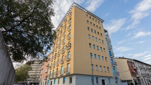 Een meerlaags woongebouw met balkons, geparkeerde auto's en een heldere lucht.