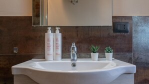 Een badkamer met een witte wastafel, twee witte flessen, een spiegel, een kraan en twee kleine planten in potten.