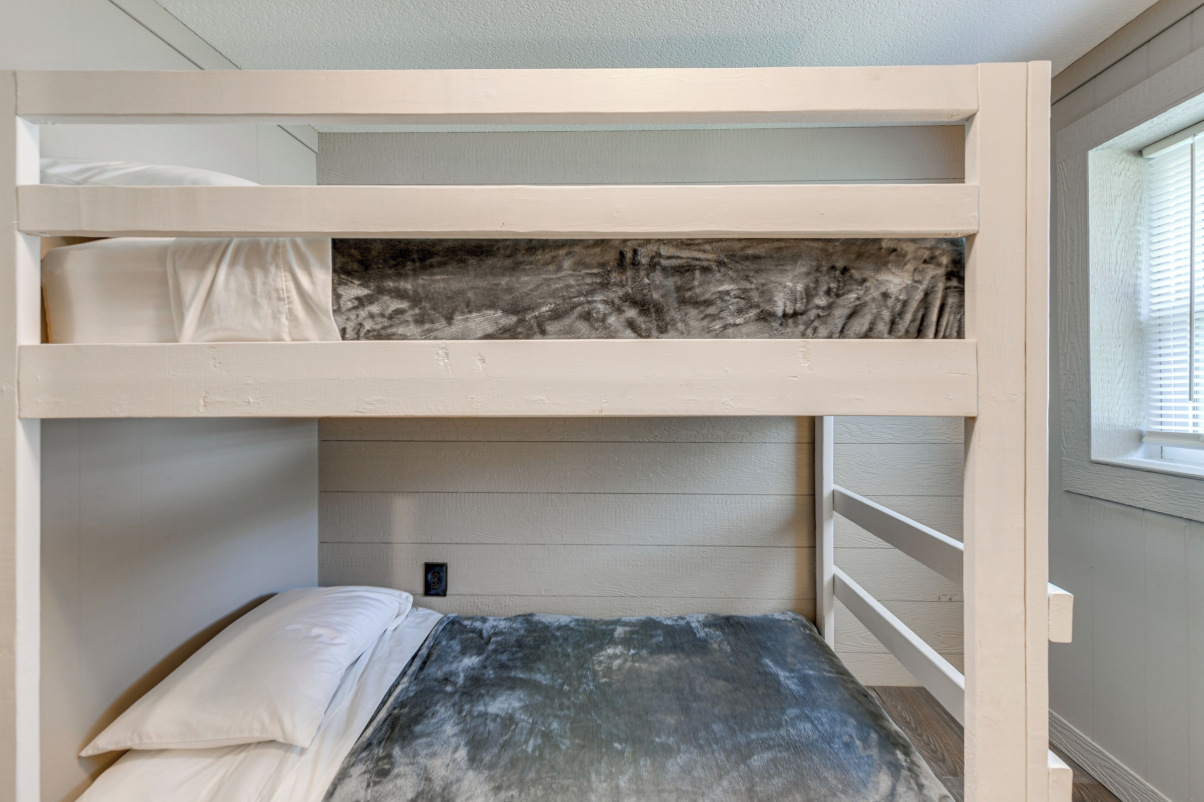 A bunk bed with a marble headboard, a small bedside table, and a window with blinds.