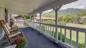 Une véranda couverte avec vue sur une montagne, une chaise berçante en bois et un pot de fleurs.
