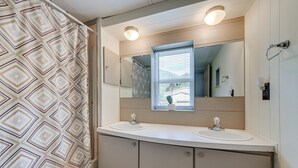 Une salle de bain avec deux lavabos, un grand miroir et une fenêtre avec des stores.