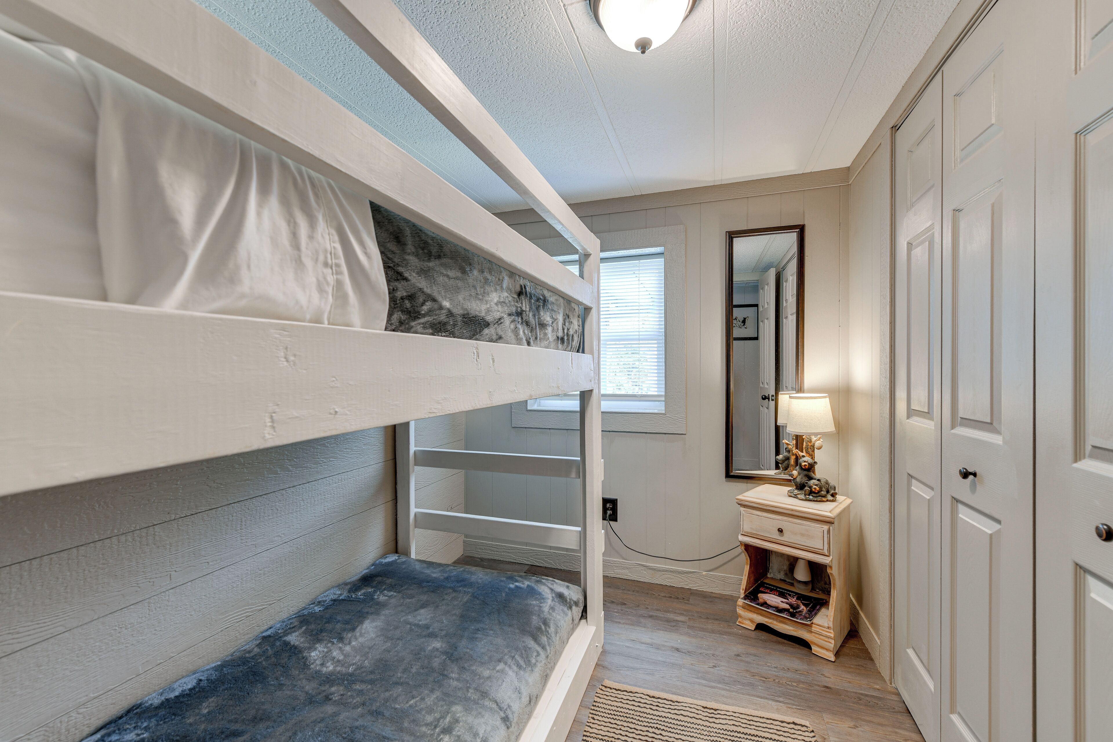 A bunk bed room with a bedside table, a mirror, and a wardrobe.