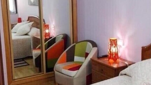 A hotel room with a bed, a chair, a nightstand with a lamp, a wardrobe, and a mirror. - Loft Amplio con Garaje en Calle Rey Aurelio en Cangas de Onís (Cangas de Onís)