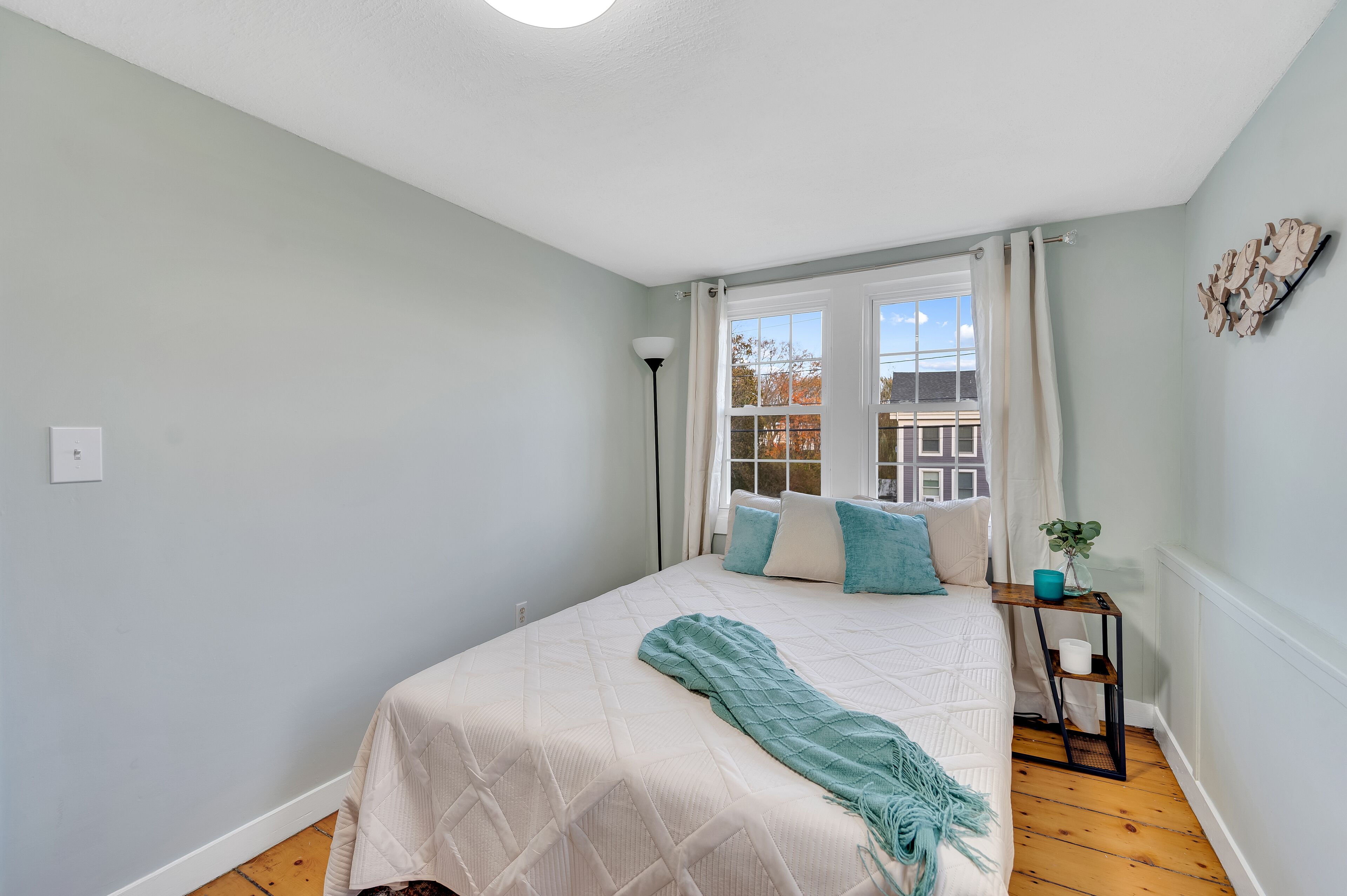 A bedroom with a bed, a nightstand, a window with curtains, and a view of buildings outside.