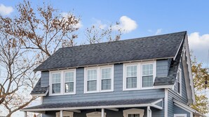 A two-story house with a porch, multiple windows, and a front door. - Adorable Cottage with Cottage porch, walk to water & town (Westbrook)