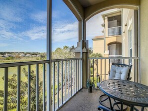 A balcony with a table and chair, overlooking a residential area with houses and greenery.
