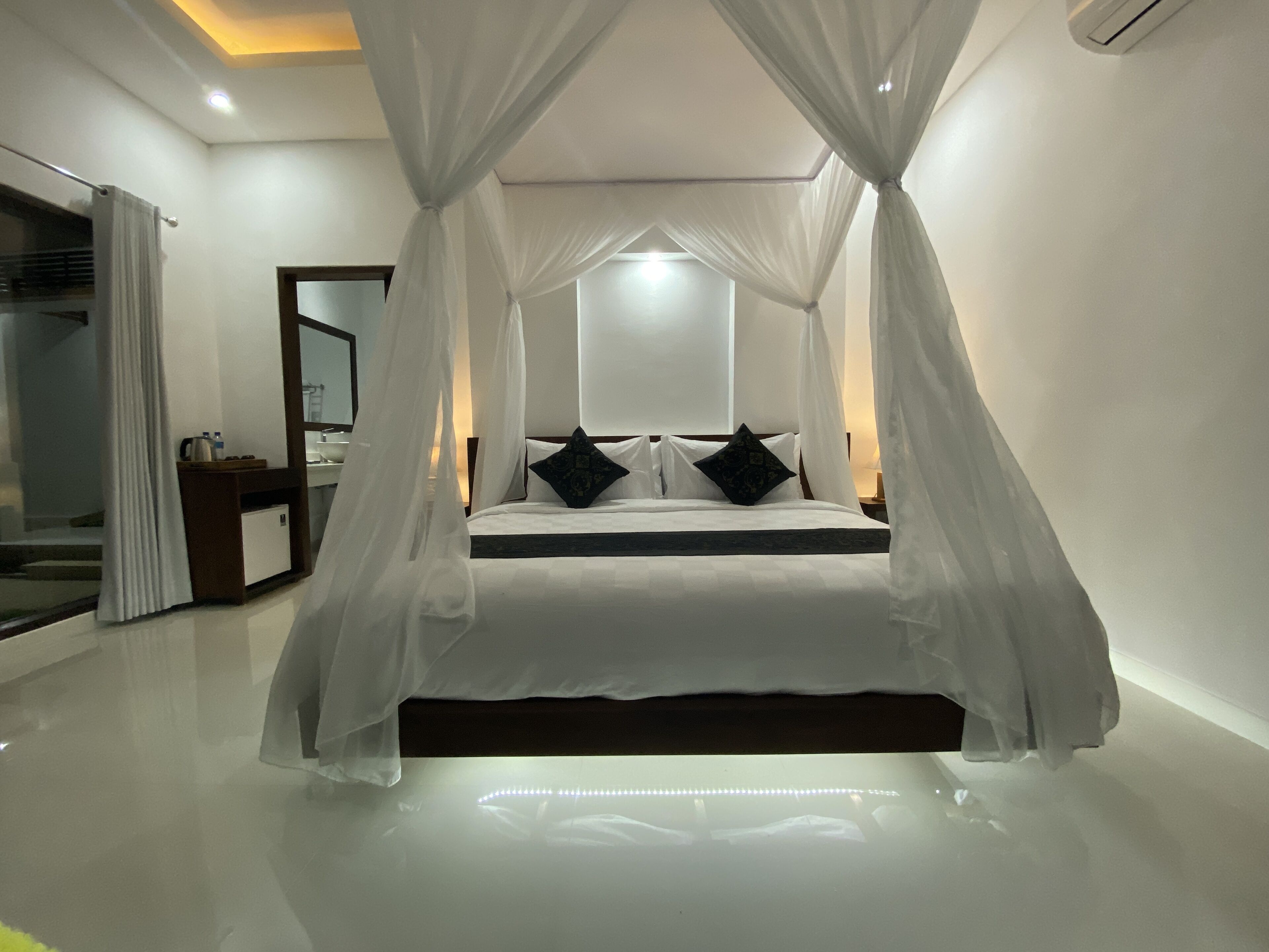 A bedroom with a canopy bed, a bedside table, a mirror, and a nightstand.