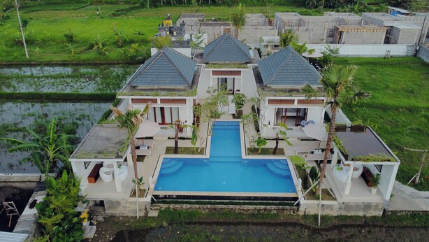 Una casa grande con piscina central, rodeada de exuberante follaje y un pequeño estanque.