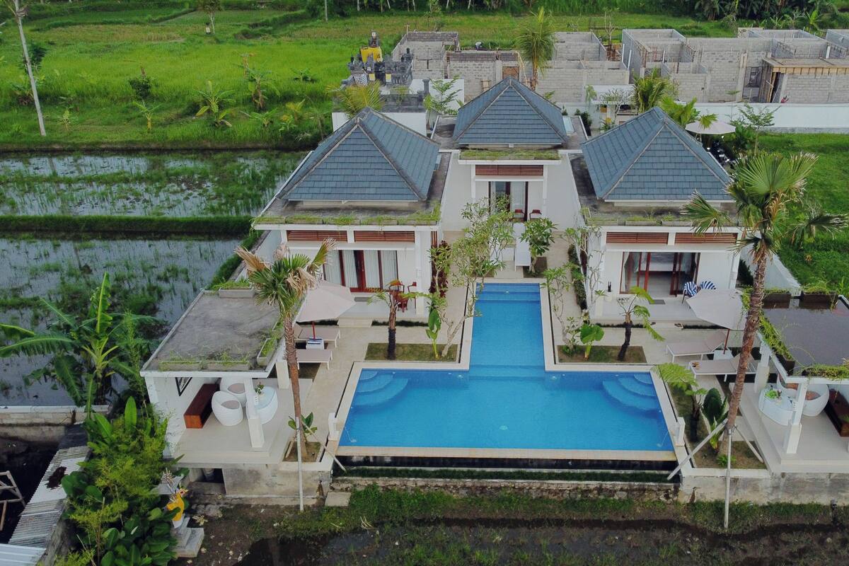 A large house with a central swimming pool, surrounded by lush greenery and a small pond.