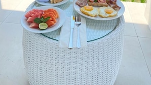 Una mesa con alimentos para el desayuno, un vaso de jugo de naranja y vistas a un campo de arroz.