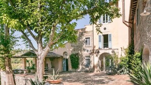 A courtyard with a pergola, potted plants, and a stone wall. - Painter's Garden (Toscana)