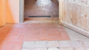 A hallway with a tiled floor, a wooden door, and a view into a room with a bed and window. - Painter's Garden (Toscana)