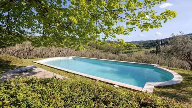 A rectangular swimming pool with a curved edge, surrounded by lush greenery and trees. - Painter's Garden (Toscana)