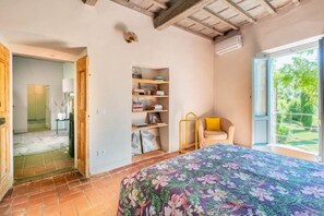A bedroom with a bed, a bookshelf, a chair, and a window with a view of greenery.