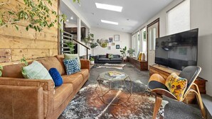 Una sala de estar con un sofá marrón, una mesa de centro de vidrio, un sofá negro, un televisor y una silla de madera.