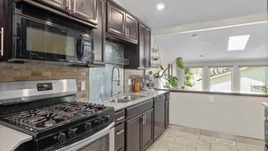 Una cocina moderna con armarios oscuros, una estufa de acero inoxidable, un microondas y una cocina a gas.
