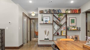 Un comedor con una mesa de madera, sillas y una estantería con libros y objetos decorativos.