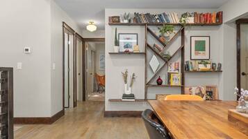 Un comedor con una mesa de madera, sillas y una estantería con libros y objetos decorativos.