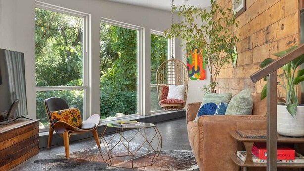 Una sala de estar moderna con ventanas amplias, una silla colgante, un sofá y una pared de madera.