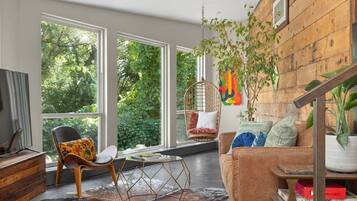 Una sala de estar moderna con ventanas amplias, una silla colgante, un sofá y una pared de madera.