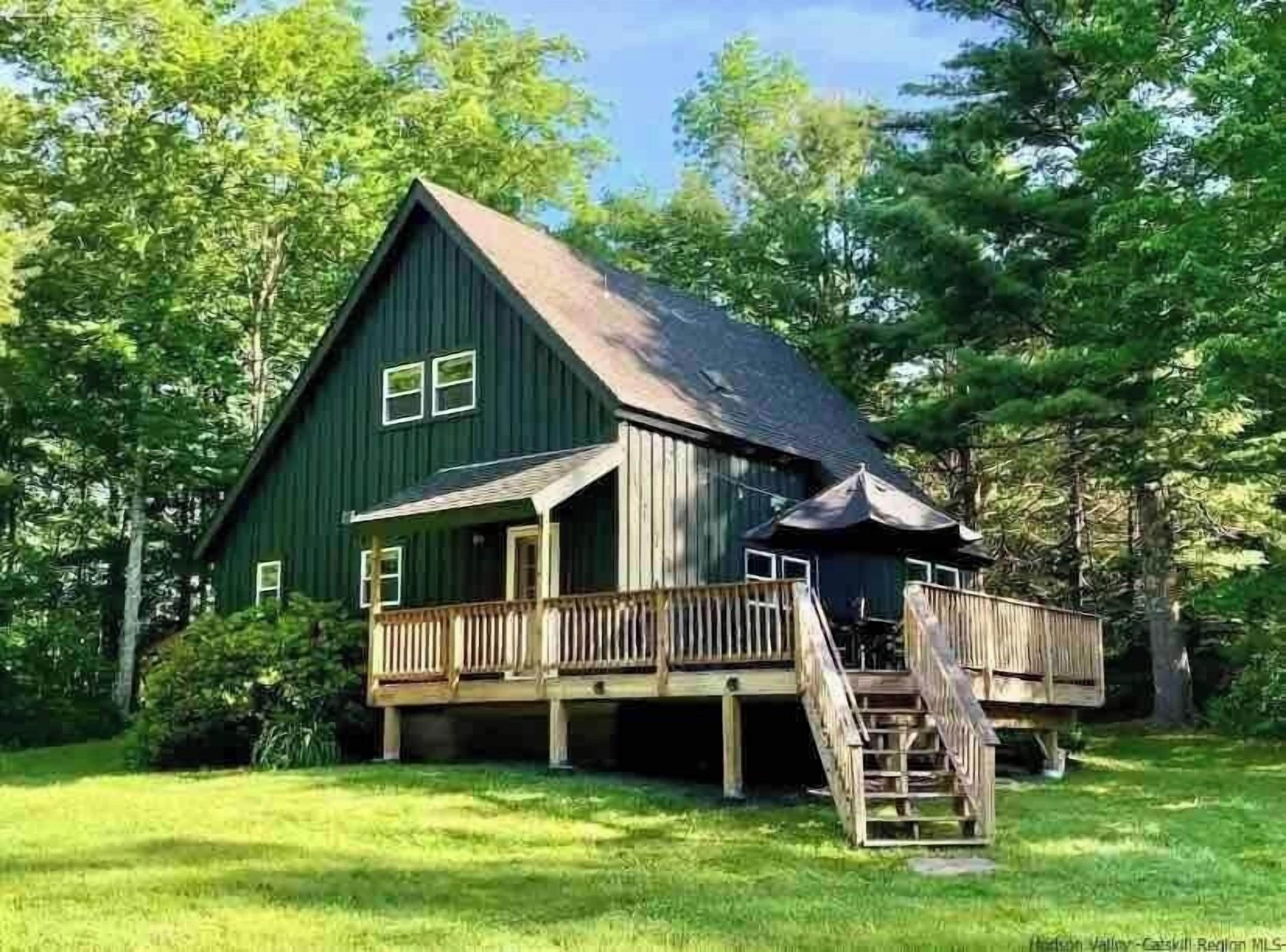 A green wooden cabin with a porch and a staircase leading to a deck.
