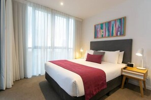 Quarto de hotel com cama grande, mesa de cabeceira com abajur e quadro na parede.