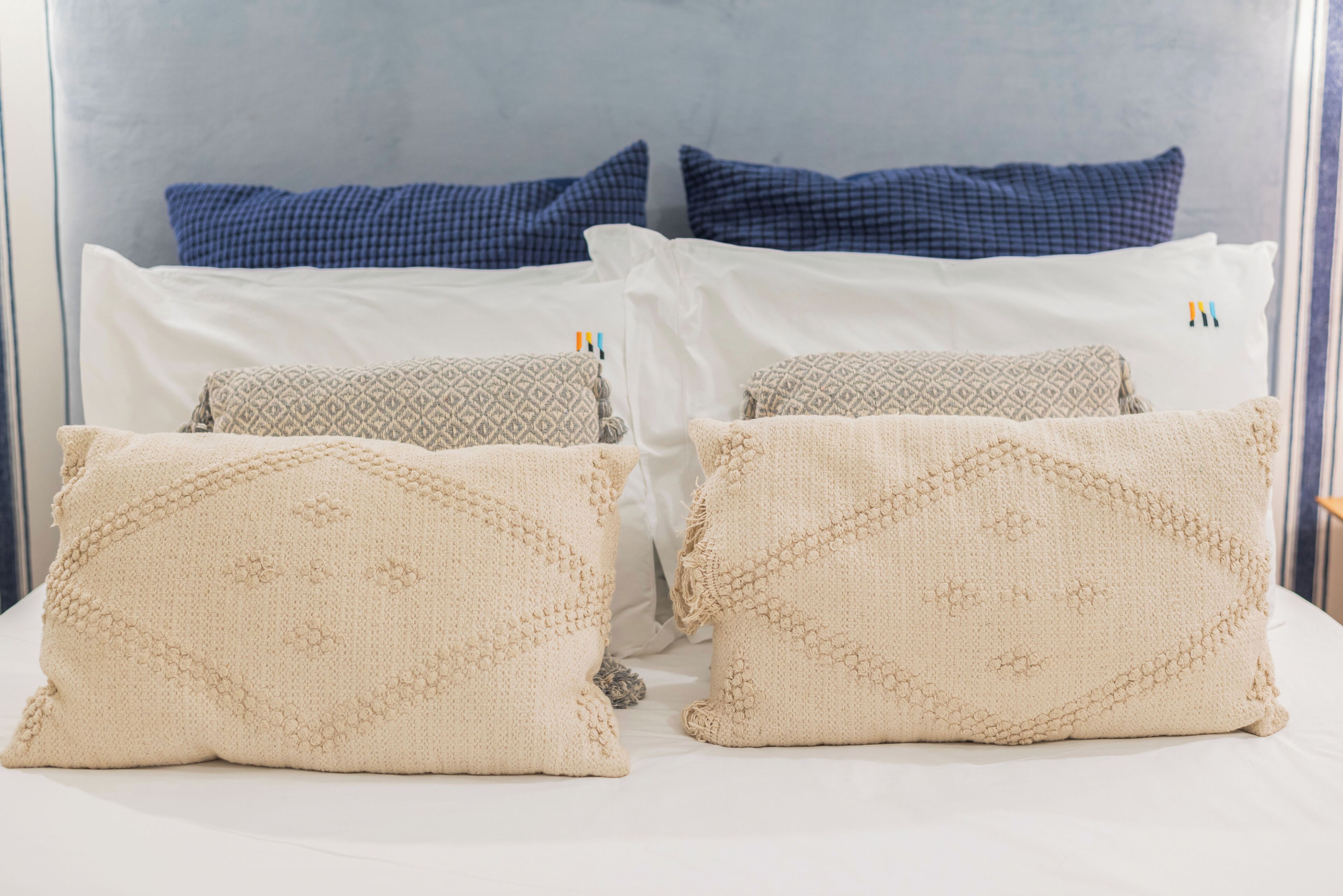 A bed with four pillows, two blue and two beige, and a headboard.