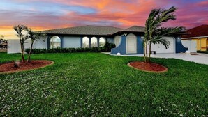 A house with a blue exterior, a grey roof, and a well-maintained lawn with palm trees. - Villa Carmen (Cape Coral)
