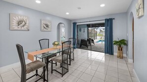A dining area with a glass table and chairs, a potted plant, and a view of a pool through a glass door. - Villa Carmen (Cape Coral)
