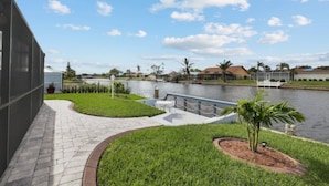 A riverside walkway with a paved path, grassy areas, and a small palm tree. - Villa Carmen (Cape Coral)