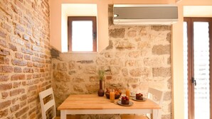 A cozy dining area with a wooden table, white chairs, and a stone wall. - Villa Rosa Suite by CorfuEscapes (Corfu)