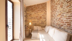 A cozy room with a brick wall, a sofa, a lamp, and a window with curtains. - Villa Rosa Suite by CorfuEscapes (Corfu)