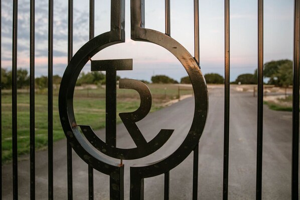 A metal gate with a circular emblem featuring a letter 'R'. - Contemporary Waterfront Ranch Villa at Twin Canyons Longhorn Ranch (Granbury)