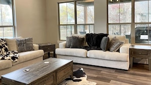 A spacious living room with a large window, a sofa, a coffee table, and a fireplace. - Contemporary Waterfront Ranch Villa at Twin Canyons Longhorn Ranch (Granbury)