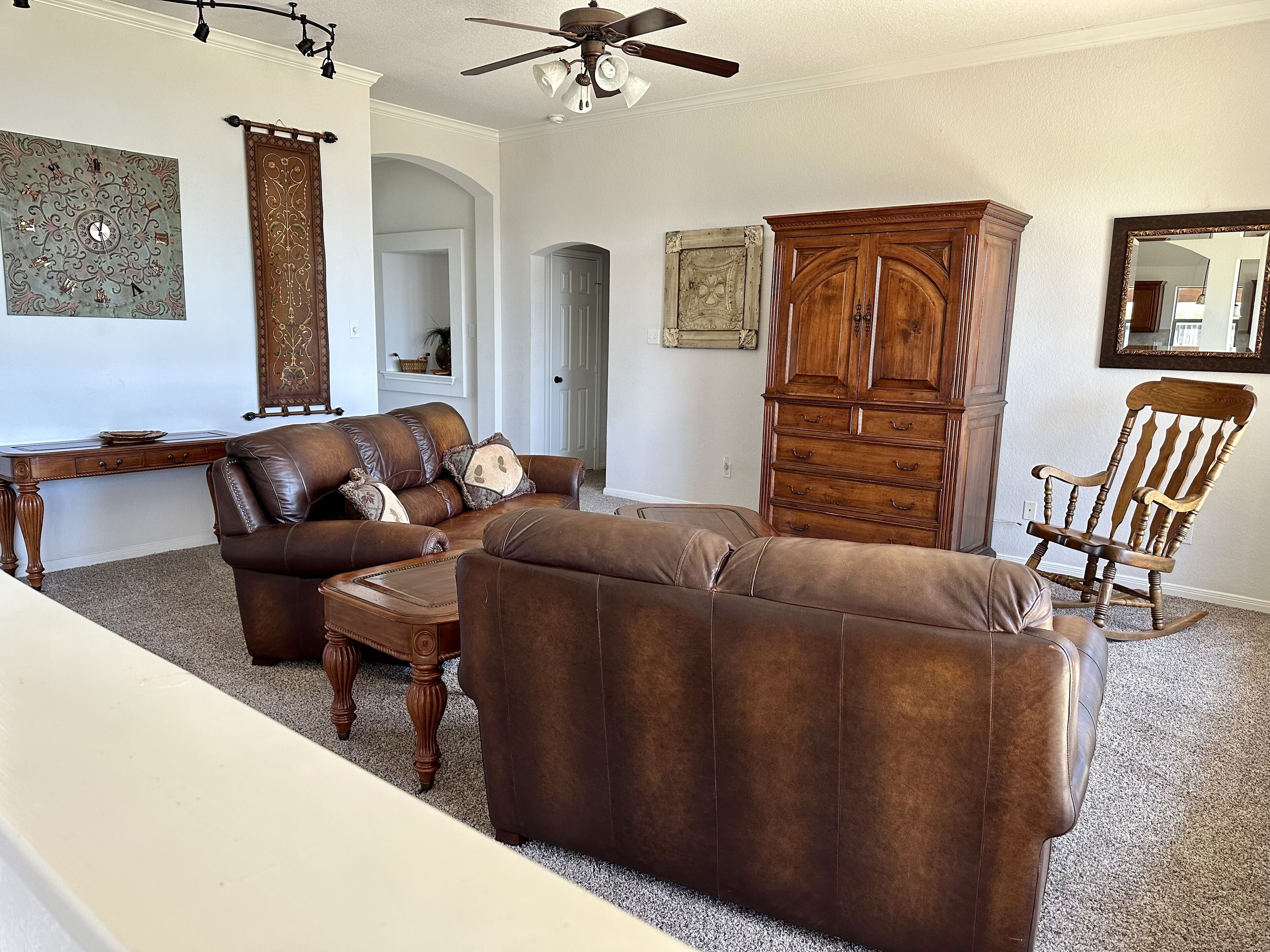 A living room with a brown leather sofa, a wooden cabinet, a rocking chair, and a ceiling fan.
