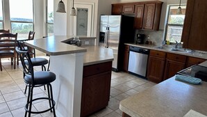 Una cocina con isla central, armarios de madera, electrodomésticos de acero inoxidable y un comedor con taburetes de bar.