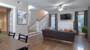 A modern living room with a wooden dining table, a sofa, and a staircase leading to another level. - 3BR Old Mansion in Montrose! Downtown, Medical Center (Houston)